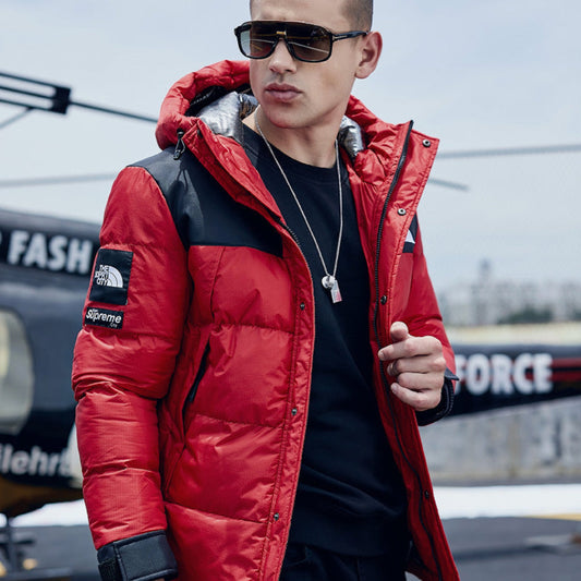 Man wearing a red thick down padded jacket, standing next to a helicopter.