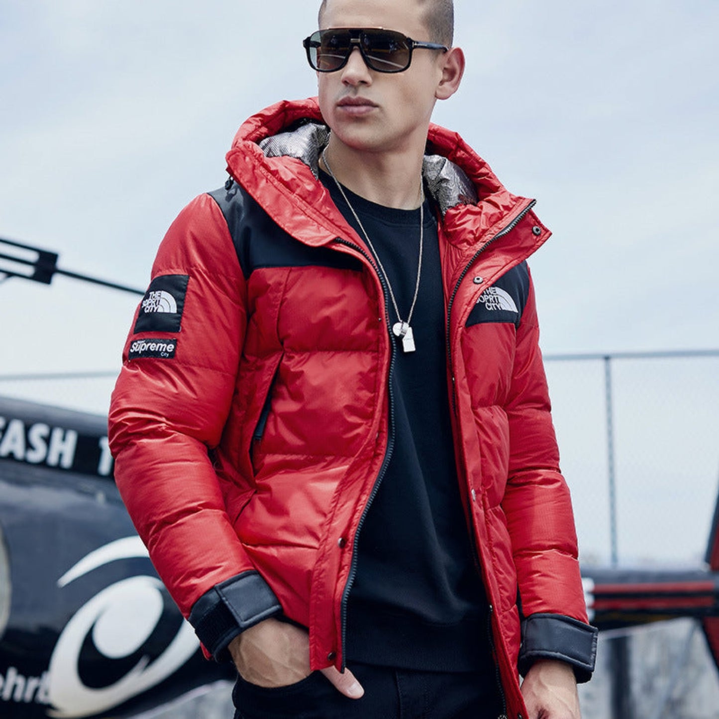 Man posing in a red jacket with sleek sunglasses and a casual outfit.