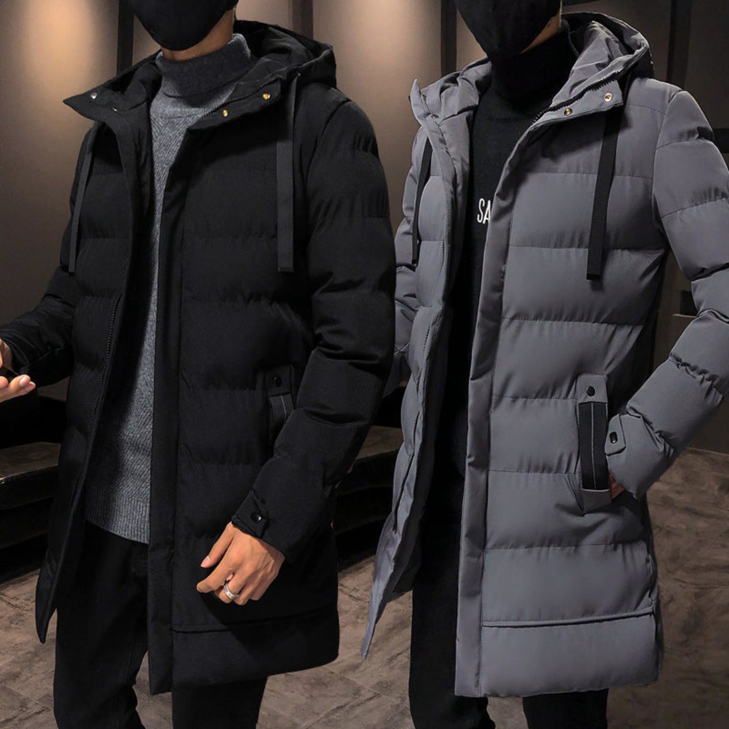 Two models side by side, wearing black and gray puffer jackets with hoods, showcasing the front view in a casual indoor setting.