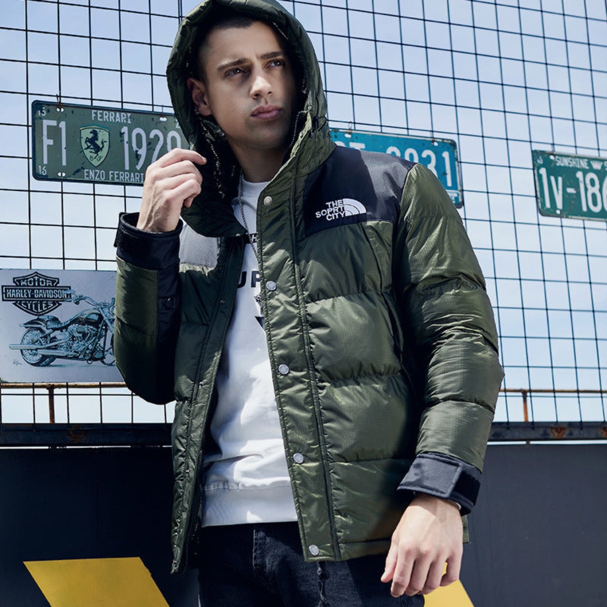 Man wearing an army green padded jacket, styled with a hoodie, standing confidently.