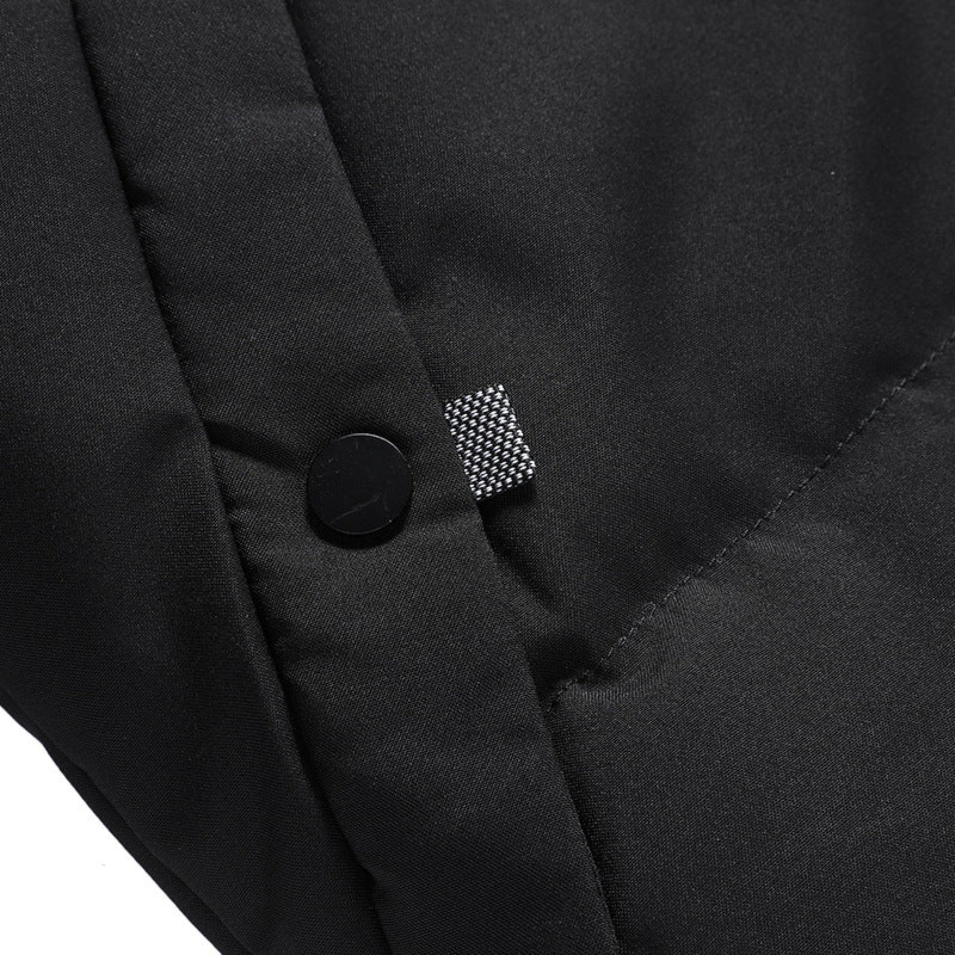 Close-up view of the black padded winter jacket's buttoned pocket detailing.