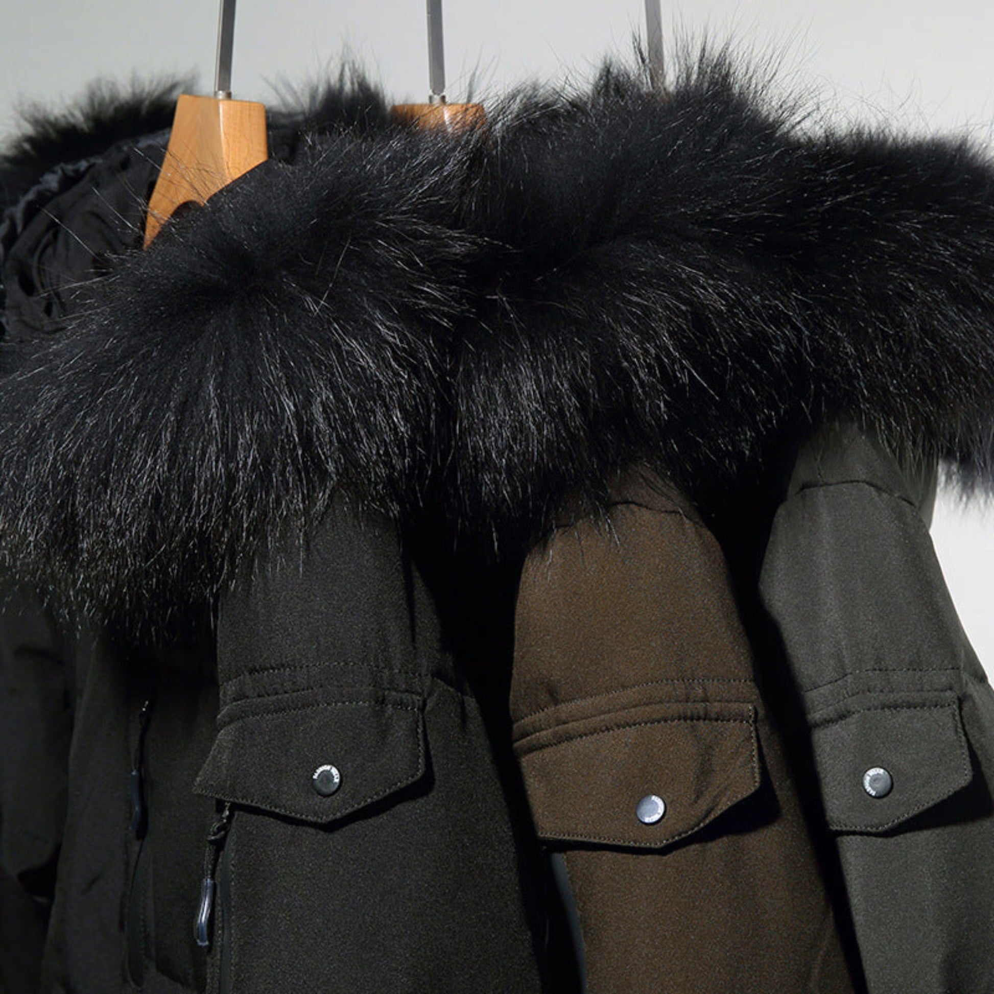 Black, grey, and green winter coats hanging on a rack, showcasing faux fur collars.